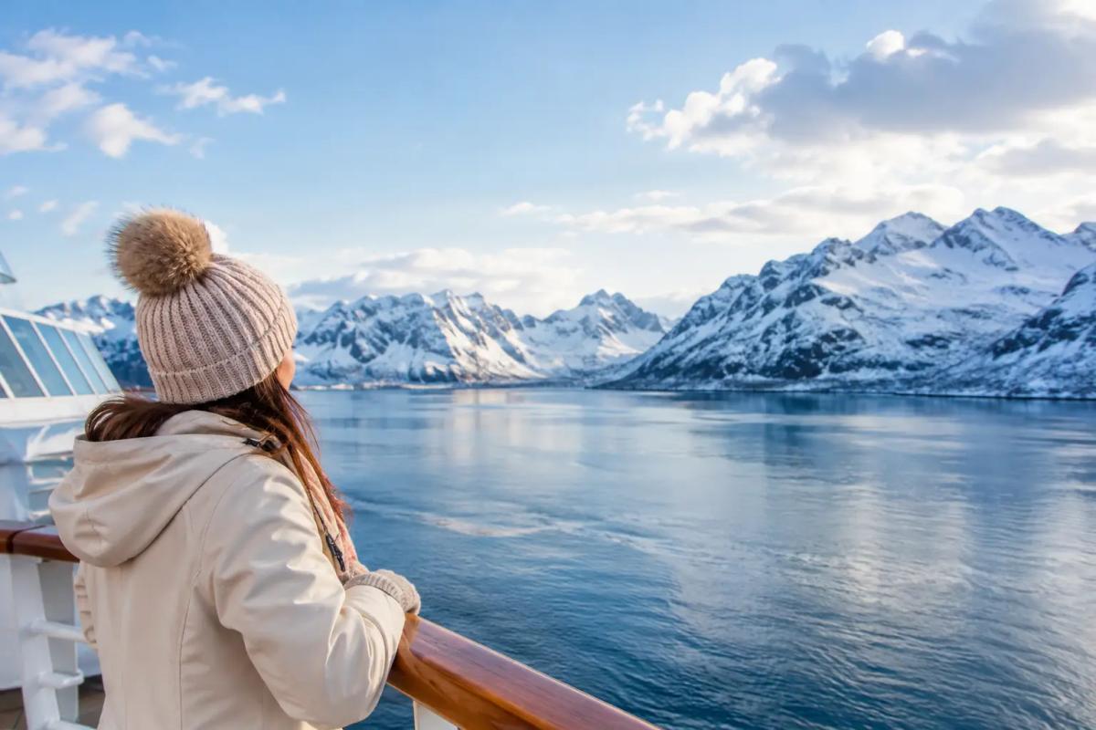 Die besten Kreuzfahrtziele im Winter Kreuzfahrtschiff bei Sonnenuntergang vor einer Palmenküste, daneben verschneite Berge
