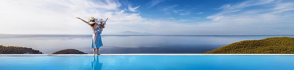 Frau mit Kind auf dem Arm von hinten mit Blick auf den Pool und das blaue Meer