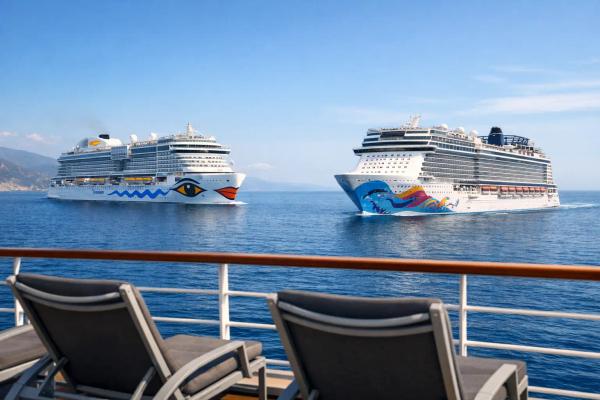 AIDA oder Norwegian Cruise Line: Sprache, Kosten, Routen Ein AIDA-Schiff und ein Schiff von Norwegian Cruise Line nebeneinander auf See, im Vordergrund Liegestühle an der Reling