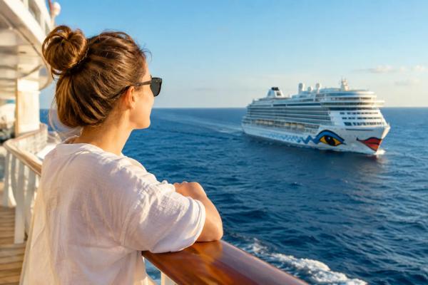 AIDA Routen Erfahrungen AIDA-Kreuzfahrtschiff auf See, im Hintergrund eine Küste mit Hafenstadt