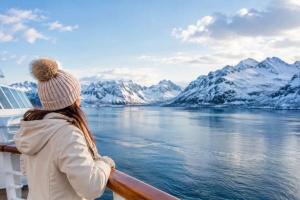 Kreuzfahrtschiff bei Sonnenuntergang vor einer Palmenküste, daneben verschneite Berge