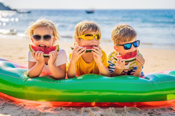 Kinder essen am Strand auf Luftmatratze Wassermelone 