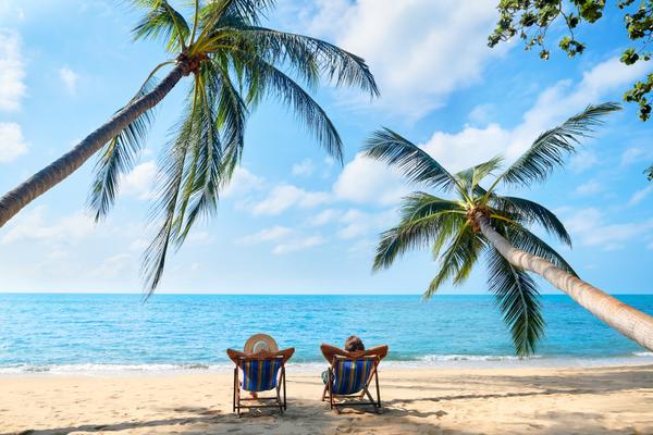 Strandurlaub zwei Personen auf Liegestühlen unter Palmen